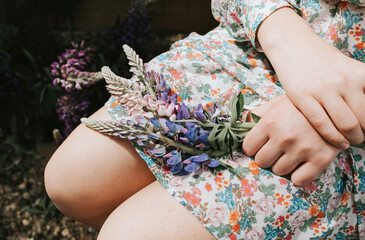 beautiful teen girl in a dress with summer bouquet of lupins on her knees in hands on a white veranda with flowers, a concept of summer vacation and a simple living