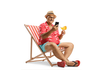 Mature male tourist sitting in a chair holding a cocktail and a smartphone