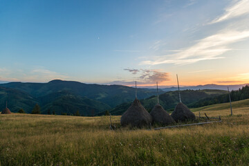 Country summer mountain rural landscape with haycocks, fields and evening sky
