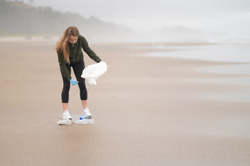 A young blonde woman, a volunteer, cleans up the debris on the ocean shore, which was taken out by the waves. Involvement in the problem of environmental pollution.