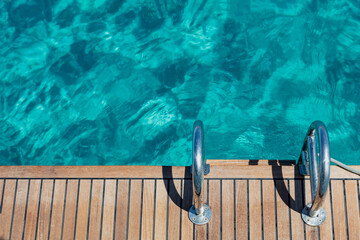 Sailing boat stern deck, teak wood and metal ladders, turquoise blue sea water background.