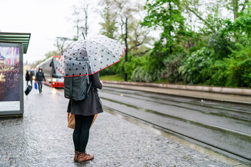 Rainy day, people wainting on tramway with umbrella.