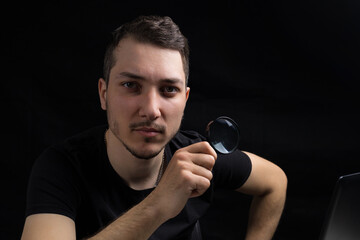 Young handsome man and a magnifying glass on black background in low key. Search symbol....
