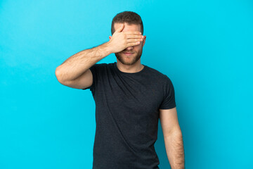 Young handsome caucasian man isolated on blue background covering eyes by hands. Do not want to see...