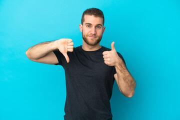 Young handsome caucasian man isolated on blue background making good-bad sign. Undecided between yes or not