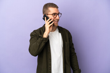 Young handsome caucasian man isolated on purple background keeping a conversation with the mobile phone