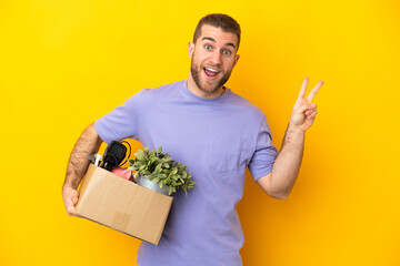 Young caucasian making a move while picking up a box full of things isolated on yellow background...