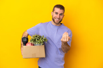 Young caucasian making a move while picking up a box full of things isolated on yellow background...