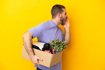 Young caucasian making a move while picking up a box full of things isolated on yellow background...