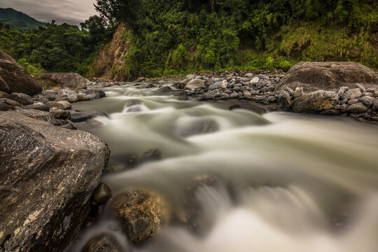 Smooth waters in a mountain river going down from with a lot of wild vegetation and grey rocks on a cloudy day. Tucumán Province, Argentina.
