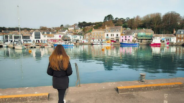 A girl looking at Padstow Harbour, Cornwall, England by River Camel in 4K.  A young woman watching at Many ships, boats and nautical vessels with beautiful English Restaurants, Pubs and cafes. 