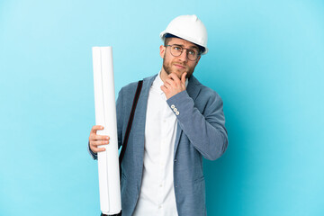 Young architect man with helmet and holding blueprints over isolated background and looking up