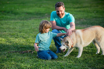 Father and son playing with dog in the garden. Dad and child with pet having fun outdoors.