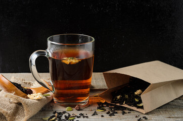 A glass mug of fragrant brewed flower tea on a wooden table, with tea leaves in a paper package, in a rustic style.