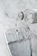 Clear drinking carbonated water is poured into glass on light background. Plastic bottle, splash,...