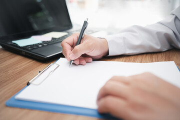 Man use pencil white document on table and use laptop computer in background