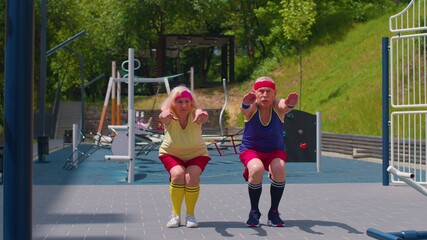 Healthy senior attractive man woman doing active training stretching muscles squatting fitness exercising outdoors on basketball playground. Active pensioners family. Elderly grandparents old couple