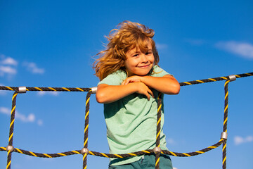 Beautiful smiling cute boy on a playground. Kids activities. Kid climbing on the net. Child sport.