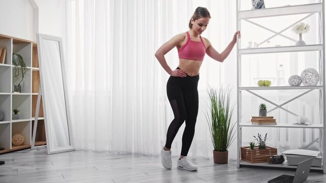 Female fitness. Sport indoors. Home workout. Fat burning. Happy sporty young woman athlete in activewear doing leg exercise in light apartment interior.
