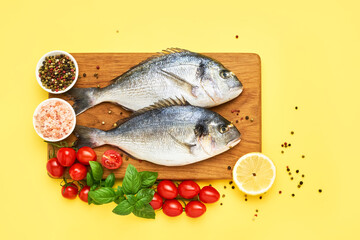 Raw dorado fish with spices on a wooden cutting board on a bright yellow background. Mediterranean seafood concept