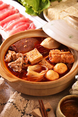 Personal spicy hot pot with pork, tofu,  mushrooms and green leaves 