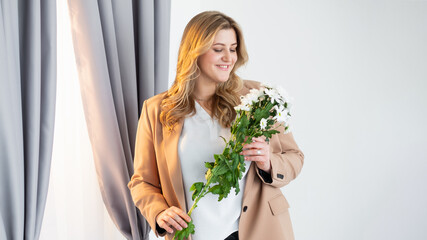 Holiday surprise. Mother day. Body positive. Natural present. Happy smiling overweight obese woman with white flowers bouquet in light room interior.