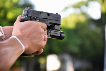 Automatic 9mm pistol which has flashlight under the muzzle holding in hand and ready to shoot, natural blurred background.