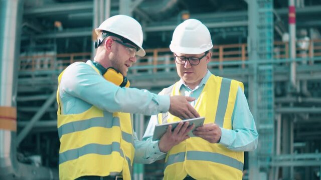 Oil industry, petrochemical factory, refinery concept. Engineers in hardhats are talking at the oil refinery