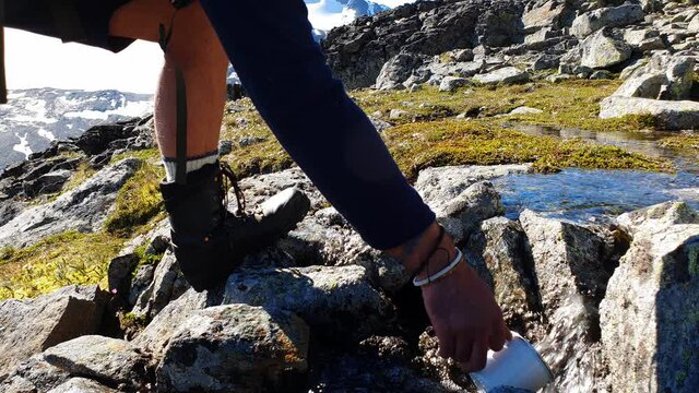 Hiker fills his enamel cup with  water from a creek - on mountain top  at Jotunheimen National Park Norway 
