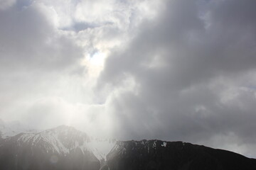 曇天のわずかな隙間から射す光が、雪山を照らす風景