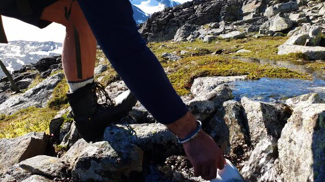 Hiker fills his enamel cup with  water  from a creek and pours it out a couple of times - on mountain top  at Jotunheimen National Park Norway 