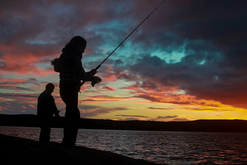 Two silhouetted people fishing  at an Esperance lake, during a vibrant and colorful sunset. 