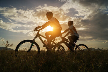 Obraz na płótnie Canvas Young Couple in love fun and happy riding mountain bike after covid-19 coronavirus outbreak. End of the coronavirus outbreak. Silhouette cycling man and woman riding mountain bike at sunset time.