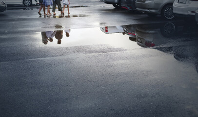 Wet parking spaces after hard rain fall with reflection of cars and walking people in puddle on the...