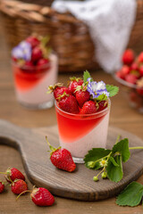 Creamy dessert with strawberry jelly in a glass with strawberry berry decor on a wooden background