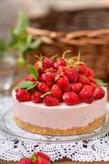 Strawberry cheesecake with a decor of a large number of strawberries and violet flowers lying on a lace napkin on a wooden background