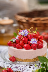 Strawberry cheesecake with a decor of a large number of strawberries and violet flowers lying on a lace napkin on a wooden background