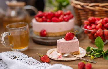A piece of cheesecake lying on a plate next to a cup of sea buckthorn tea on the background of a whole cake