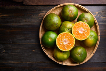 Green tangerine orange fruit in a bamboo basket on wooden background, Table top view