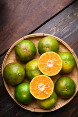 Green tangerine orange fruit in a bamboo basket on wooden background, Table top view