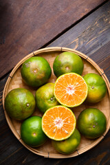 Naklejka na ściany i meble Green tangerine orange fruit in a bamboo basket on wooden background, Table top view