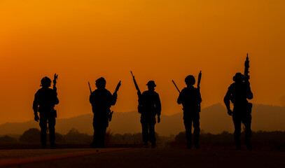 Fototapeta na wymiar The military silhouettes of soldiers hold gun against with sunset sky background