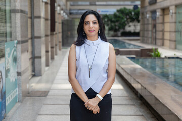 An Indian woman standing with her arms crossed in an urban corporate setting. Corporate female in smart formal attire