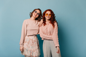 Adorable girls in sunglasses looking at camera. Front view of smiling friends isolated on blue background.