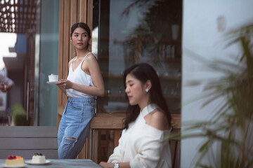 Two pretty young women enjoying coffee and cake together in a coffee house sitting at a table laughing and gossiping with happy smiles.