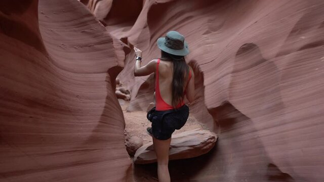 Back of young woman with photo camera walking in a narrow slot sandstone canyon, amazing landscape and natural beauty of Antelope Canyon, Arizona USA, slow motion