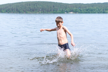 Cute happy boy makes water splash in the lake. The child runs through the water creating splashes.