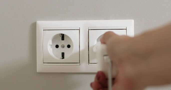 Woman's hand plugging white power plug into white multiple socket indoors.