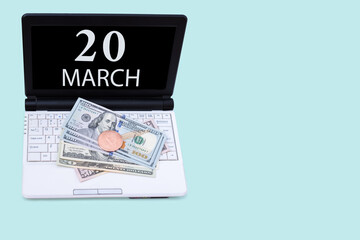 Obraz premium Laptop with the date of 20 march and cryptocurrency Bitcoin, dollars on a blue background. Buy or sell cryptocurrency. Stock market concept.