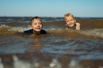 7-8 years old cute caucasian boys swim in the sea with big splashes. Children enjoys swimming in the ocean. Holidays, vacation with kids.